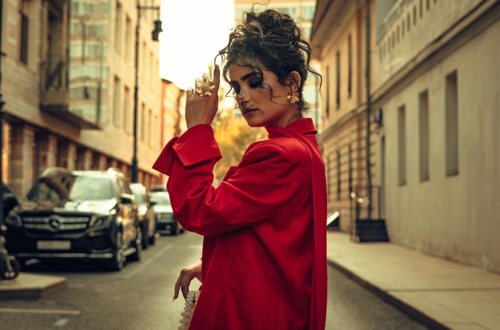 Fashionable woman in a red dress posing confidently on an urban street.