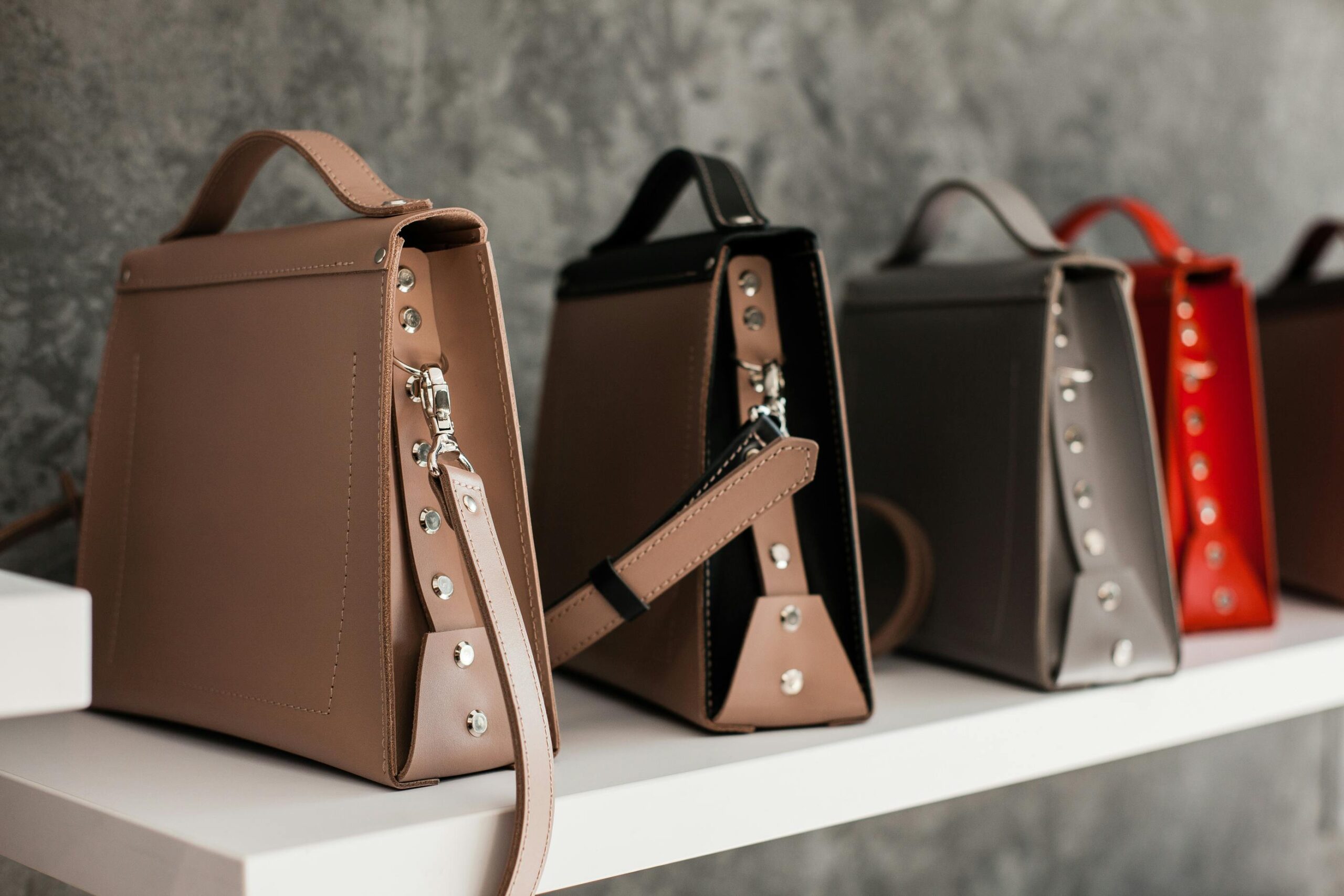 Luxury leather handbags displayed on a white shelf, showcasing minimalistic design and various colors.